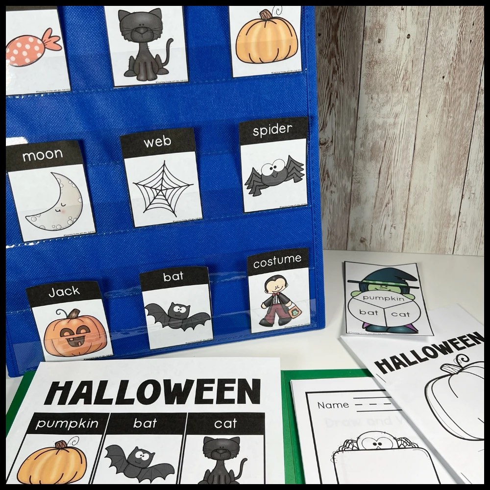 Halloween word cards with pictures in a pocket chart, next to a Halloween word poster and writing pages