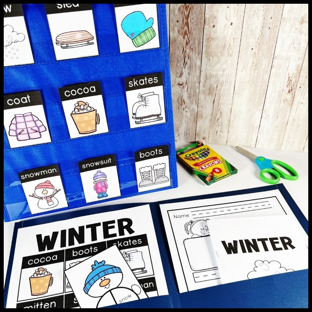 Winter word cards like coat, cocoa, skates and snowman in a blue pocket chart beside a winter writing folder